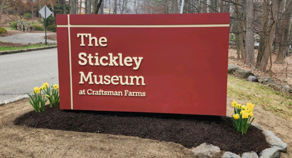 New Entrance Sign to The Stickley Museum at Craftsman Farms with several yellow daffodils planted at the base.