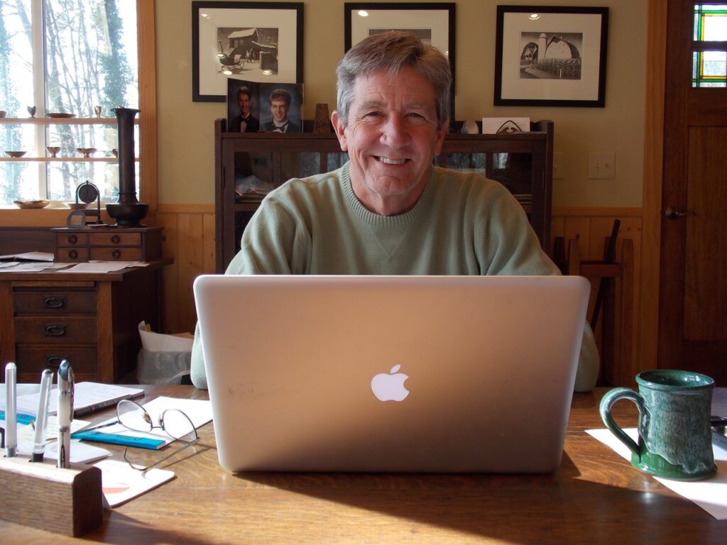 Bruce Johnson, seated at an oak desk with an open macbook and a ceramic coffee mug.