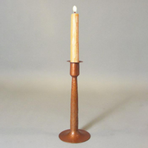 Single hand-hammered copper candlestick with a lit candle in it centered on a grey background.