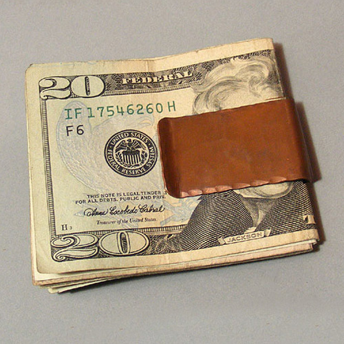 This image shows a copper money clip on some twenty dollar bills.