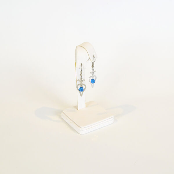 This image shows our Gibson Girl Heart Earrings that are silver with a blue bead hanging within the heart displayed on a single earring holder