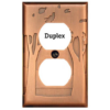 This image shows a duplex style copper light switch plate by James Matteson in the landscape design. One large tree can be found on the left and right side of the outlet cover.