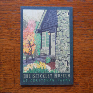 This image shows the front of the wooden postcard featuring Julie Leidel's print The Stickley Museum at Craftsman Farms against a wood background.