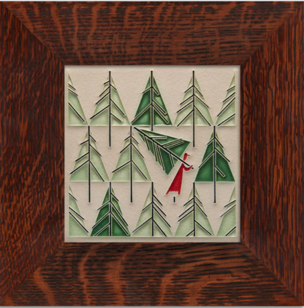 This image shows the framed Perfect Tree from Motawi. The frame is brown oak. The tile itself shows light and dark green trees with a person in red picking up and carrying away a single tree.
