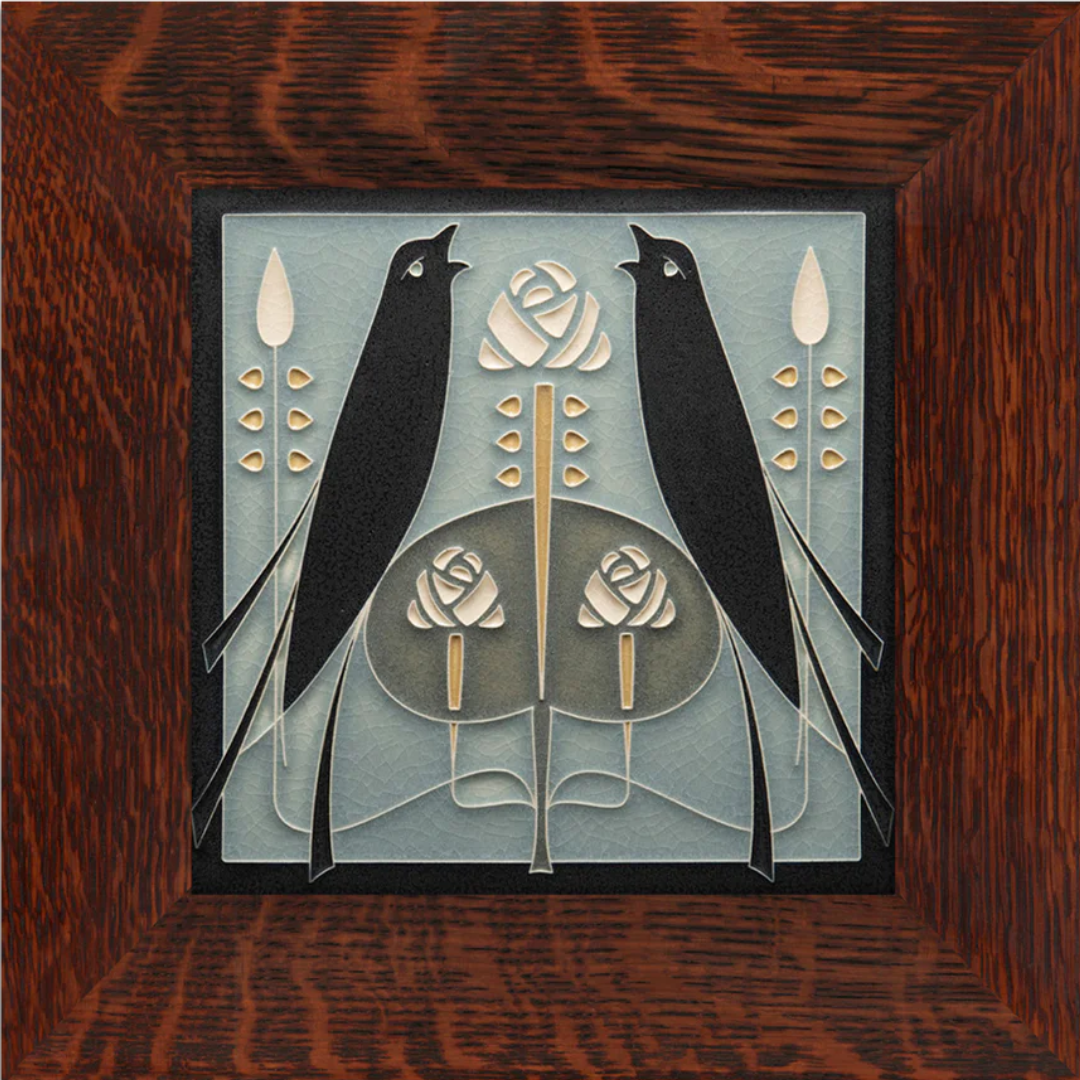 This image shows two black songbirds in a mirrored stance facing each other. There are three Macintosh roses in the tile and two others floral details in the top corners above the birds. The tile has a light blue background and is in a brown oak frame.