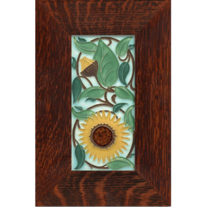 This image shows the Motawi tile in the sunflower design. It Features a yellow sunflower that fills the bottom half of the tile. The top half is filled with leaves and other sunflower buds. The background is light blue and the tile is finished in an brown oak frame.