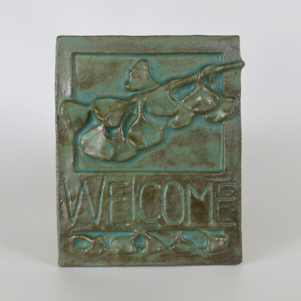 This image shows our gingko welcome time produced by Janet Ontko. The ceramic plaque is glazed in a green glaze that is more green where it is thickest and more brown where it is thin.
