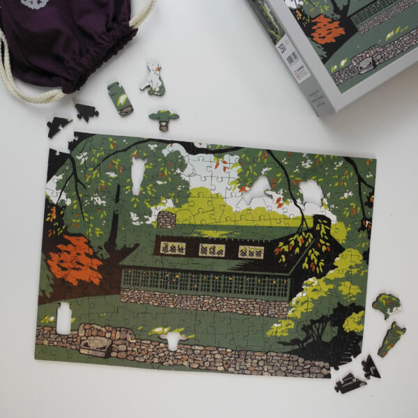 This image shows all the contents you would receive if you purchased a puzzle featuring Laura Wilder's print. This image highlights the puzzle, box and purple bag for the puzzle pieces.