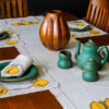 This image shows a modern Stickley Table and Chairs decorated with a beautiful tall ribbed copper vase, with our united crafts tea pot set, plates, runners, placemats and napkins on the table.